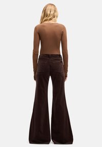 Braunes Langarmoberteil, kombiniert mit hoch taillierten, ausgestellten braunen Cordhosen mit Gesäßtaschen und dezenten Steppnähten.