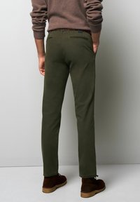 Olijfgroene katoenen broek met een slim fit, voorzien van twee achterzakken, een geweven riem met meerkleurige accenten en bruine suède schoenen.