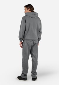 Man wearing a matching gray hoodie and sweatpants with black sneakers, standing facing away on a white background.