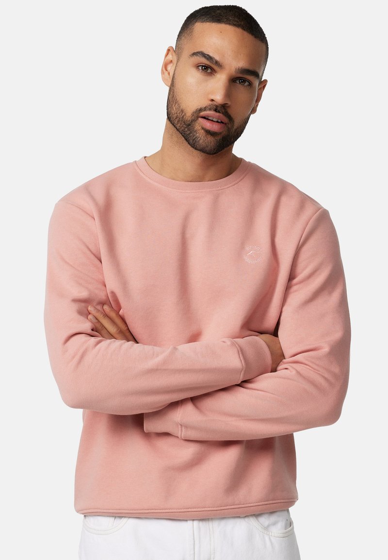 Sudadera rosa claro con cuello redondo y mangas largas, que presenta un pequeño logo en el pecho y puños y dobladillo acanalados. Textura de tejido suave.