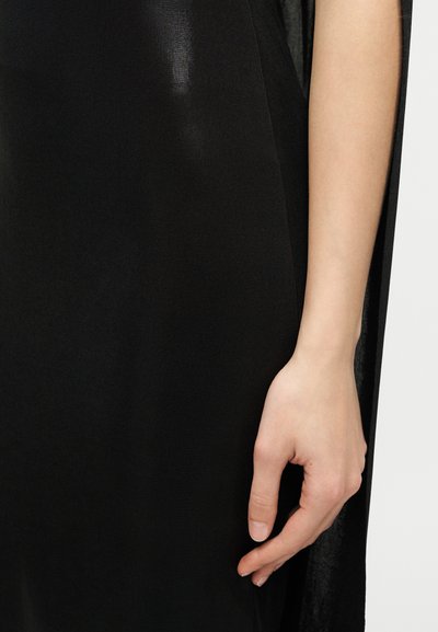 Egy személy jobb kezének közeli képe, ujjai lazán nyújtva, mellette egy fekete textilruhadarab, egyszerű világos háttéren.