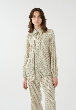 Blusa color crema con un patrón geométrico, con cuello con lazo, mangas largas y tela texturizada. Combinada con pantalones a juego con el mismo patrón.