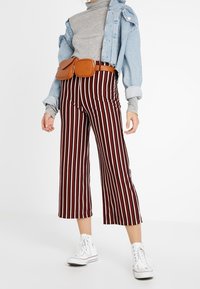 Rood en wit gestreepte culottes met een ontspannen pasvorm, gecombineerd met een grijze coltrui en een spijkerjasje. Een bruine heuptas en witte sneakers maken de look compleet.