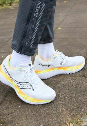 Pantofi sport albi cu o parte superioară din plasă respirabilă, accente negre și o talpă multicoloră cu degradeuri de galben și portocaliu.