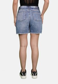 Shorts in denim azzurro chiaro, con orlo sfilacciato, due tasche posteriori e vita standard, abbinati a sneakers nere.