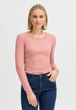 Langarmige roze ribbeltop met een met kant afgewerkte halslijn en mouwen, gecombineerd met donkerblauwe denim jeans.