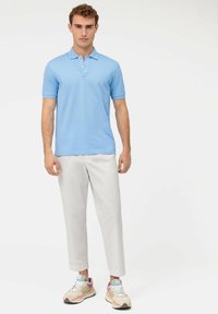 Polo shirt azzurro chiaro con maniche corte, colletto a due bottoni, abbinato a pantaloni bianchi e sneakers multicolori. Vestibilità casual.