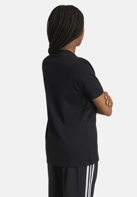 Camiseta negra de manga corta, diseño de cuello redondo, fabricada en suave algodón. Mostrada desde la parte de atrás, con un corte relajado y sin logotipos visibles.