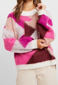 Maglione lavorato a maglia colorato con un motivo geometrico nei toni di rosa, rosso e beige, texture accogliente e colletto e polsini a costine.