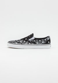 Black slip-on sneaker with white skull and swirl pattern. Canvas upper, rubber sole, and padded collar. Features stitching accents.