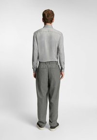 Camicia a maniche lunghe grigia chiara con una texture liscia e colletto, abbinata a pantaloni larghi grigio scuro e sneakers casual.