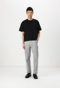 Camiseta de algodón negra de mangas cortas, combinada con pantalones gris claro y zapatos negros, sobre un fondo blanco.