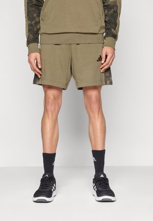 Olive green athletic shorts with textured black side accents, featuring an embroidered logo. Paired with black sneakers and socks.