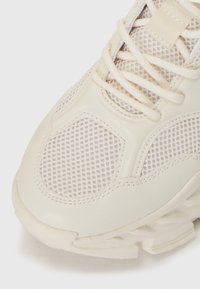Baskets chunky avec une tige synthétique de couleur crème et des panneaux en mesh. Présente des accents surélevés, des lacets plats et une semelle texturée pour l'adhérence.
