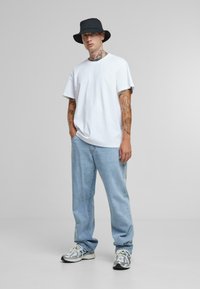Witte T-shirt met korte mouwen, lichtblauwe losse jeans, zwarte bucket hat en zilveren hardloopschoenen met zwarte accenten. Gladde stoftextuur.