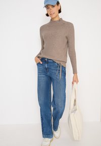 Khaki ribbed sweater z detalem na zamek, w połączeniu z niebieskimi dżinsami o prostym kroju. Trzymając białą futrzaną torbę na ramię, nosi jasnoniebieską czapkę.