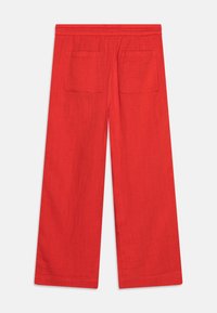 Czerwone spodnie o szerokich nogawkach z elastycznym paskiem w talii i dwiema kwadratowymi kieszeniami naszytymi z tyłu, zaprezentowane na płasko na białym tle.