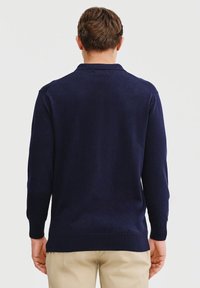Granatowy sweter dzianinowy z kołnierzem, długimi rękawami i gładką fakturą. Posiada prosty dół oraz czyste linie bez ozdób.