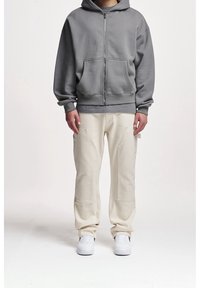 Grijze rits hoodie van katoen met een ruime pasvorm en voorzakken, gecombineerd met crèmekleurige broek met zijzakken en naden.