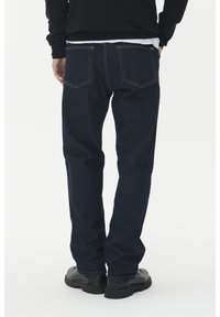 Blugi negri din denim cu un design drept, având două buzunare laterale și cusături în contrast, asortați cu pantofi negri.