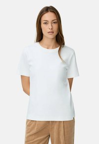 Witte T-shirt met korte mouwen en ronde hals, gemaakt van gladde stof, gecombineerd met beige corduroy broeken. Eenvoudig ontwerp, zonder patronen.