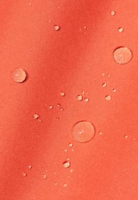 Rød, struktureret stof med flere vanddr�åber i forskellige størrelser på overfladen, der fremhæver dets vandafvisende egenskaber.