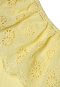 Tela amarilla con bordado floral, detalles recortados, borde en forma de onda y una superficie ligeramente texturizada.