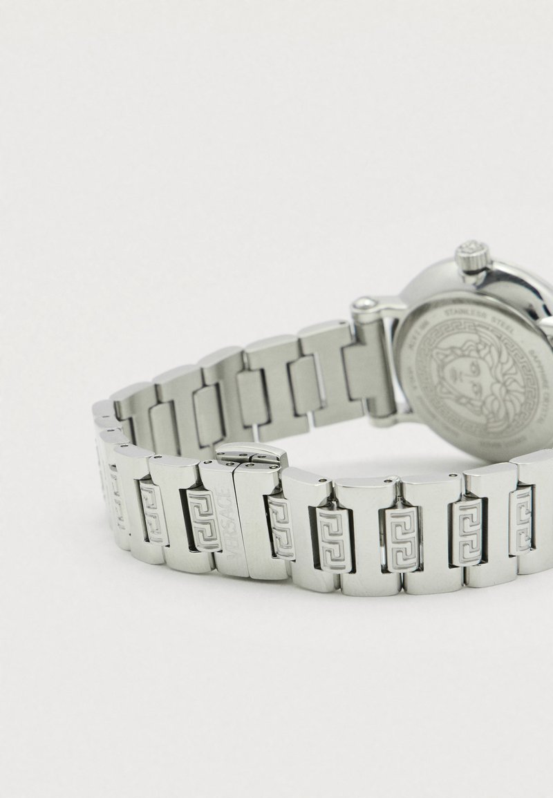 Silberne Edelstahluhr mit einem Gliederarmband, verziert mit gravierten Mustern und einem runden Gehäuse mit strukturiertem Rücken.