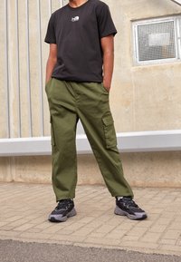 Camiseta negra de algodón con pequeño logo blanco, combinada con pantalones cargo verde oliva de corte holgado con bolsillos laterales y zapatillas negras con detalles.