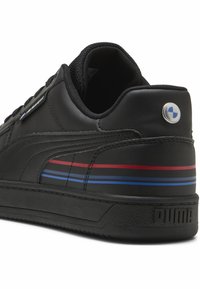 Adidași din piele neagră cu o suprafață texturată, prezentând dungi roșii și albastre, un accent cu un logo rotund și o guleră căptușită. Talpă din cauciuc.