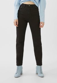 Jeans negros de talle alto con un diseño ajustado y estilo de cinco bolsillos. Combinados con botas de tacón alto y cordones en un tono azul claro.