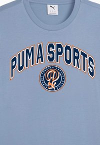 Šviesiai mėlynas medvilninis marškinėliai su ryškiu "PUMA SPORTS" užrašu jūrų mėlyna ir oranžine spalvomis, su apvaliu logotipu, kuriame yra oranžinė raidė "P" ir grafika.