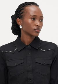 Zwarte overhemddas met twee borstzakken, versierd met studdetails op de schouders en een klassiek kraagontwerp. Glad textuur van de stof.