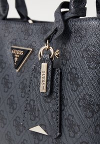 Borsa nera testurizzata con hardware dorato, caratterizzata da una placca con logo triangolare e un piccolo tag. Nota per il suo motivo in rilievo sulla superficie.