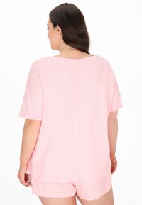 Tricou roz deschis, cu mânecă scurtă, realizat dintr-un material texturat, având detalii la cusătura din spate și o croială lejeră, asociat cu pantaloni scurți asortați.