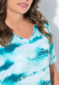 Camiseta de cuello en V en un patrón de tie-dye azul claro y verde azulado, con peces ilustrados en blanco. Mangas cortas, tela suave, diseño casual.