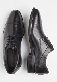 Scarpe eleganti in pelle nera con finitura liscia, punta rotonda, design con lacci e dettagli di cucitura sottili. Tacco basso e piatto.
