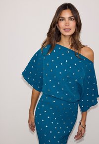 Τιρκουάζ φόρεμα με σχέδιο χωρίς τιράντες, υφή υφάσματος και χρυσές/ασημένιες πουά. Φορέματα με φουσκωτά μανίκια και εφαρμοστή σιλουέτα.