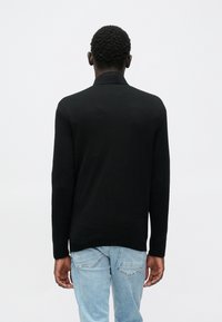 Schwarzer Pullover mit langen Ärmeln, hohem Kragen, gerippten Bündchen und Saum. Wird mit hellblauen Jeans getragen, die eine glatte Textur und eine figurbetonte Passform aufweisen.