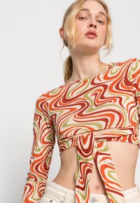 Camisola de mangas compridas tipo cropped com um padrão espiral multicolorido (laranja, vermelho, verde) e um nó na parte da frente, confeccionada em um tecido suave.