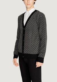 Cardigan a righe chevron nero e grigio, tessuto lavorato a maglia, vestibilità slim, scollo a V, con bottoni frontali, polsini e orlo a coste. Abbinato a pantaloni neri.