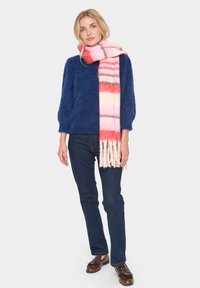 Tamsiai mėlynas pūkuotas megztinis, tamsūs džinsai ir daugiaspalvė dryžuota skara su rožinės, raudonos ir baltos atspalviais, užbaigta su kutais.