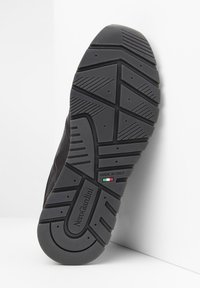 Suola di scarpa in gomma nera con pattern di battistrada testurizzato, caratterizzato da scanalature e disegni circolari. Dettaglio "Made in Italy" e bandiera italiana visibile.