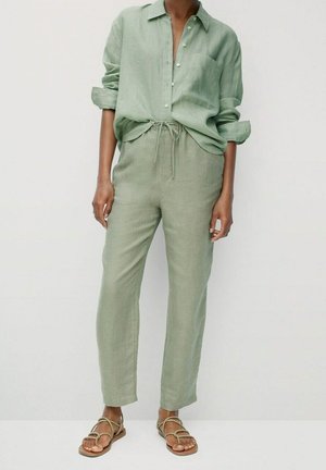 Lichtgroene linnen blouse met knopen vooraan, opgerolde mouwen; bijpassende broek met drawstring in een relaxte fit; bruine platte sandalen.