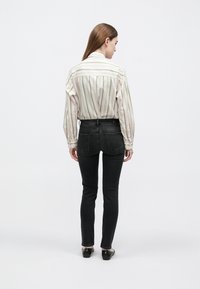 Világos színű, sárga kiemelésekkel díszített csíkos ing, fekete slim fit farmerrel, hátulról nézve. A megjelenést lapos fekete cipő teszi teljessé.