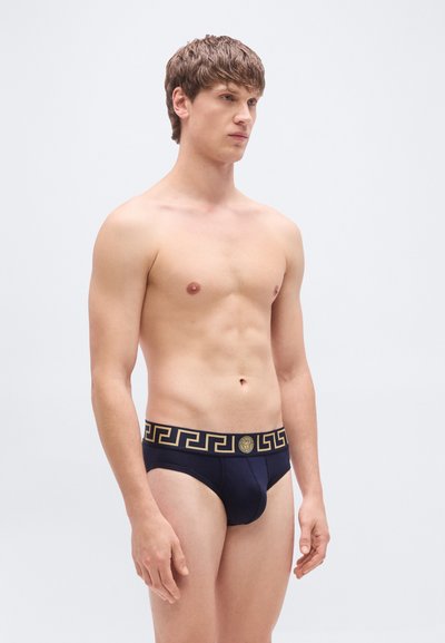 Σκούρα μπλε σλιπ με χρυσό γεωμετρικό σχέδιο στη μέση. Μαλακό υλικό, εφαρμοστό σχέδιο και χαμηλή μέση.