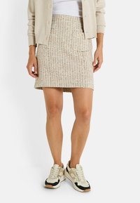 Falda de punto a cuadros en beige, con un diseño ajustado y un bolsillo trasero. Combinada con zapatillas crema y negras, que presentan detalles texturizados.