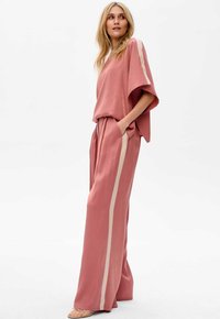 Jasno różowa, luźna bluzka oraz szerokie spodnie z beżowym paskiem po bokach. Gładka tekstura, swobodny krój i detal w postaci kieszeni w spodniach.