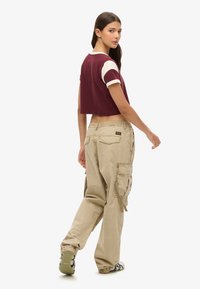 Kortere bordeauxrood T-shirt met witte mouwen en beige cargobroek met zijzakken en trekkoordboorden. Platte schoenen met patroon.