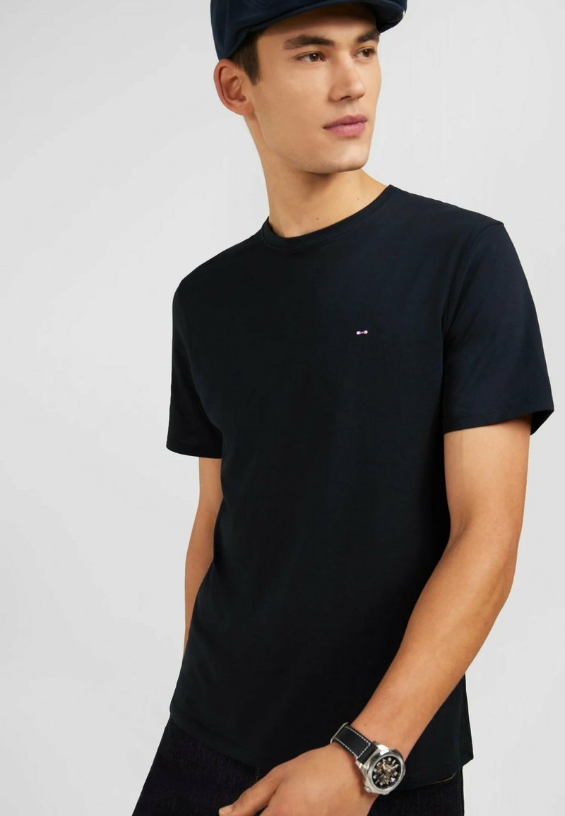 T-shirt en coton noir à manches courtes et col rond. Présente un petit logo sur la poitrine. Le tissu semble lisse et léger.